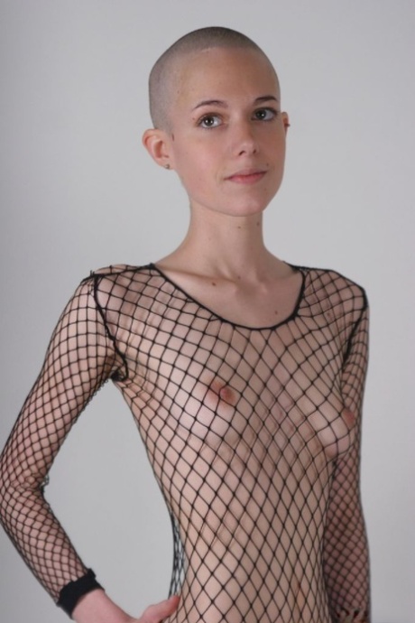 Solo model with a shaved head poses in a fishnet bodystocking