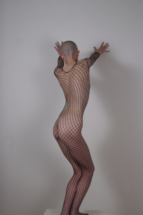 Solo model with a shaved head poses in a fishnet bodystocking