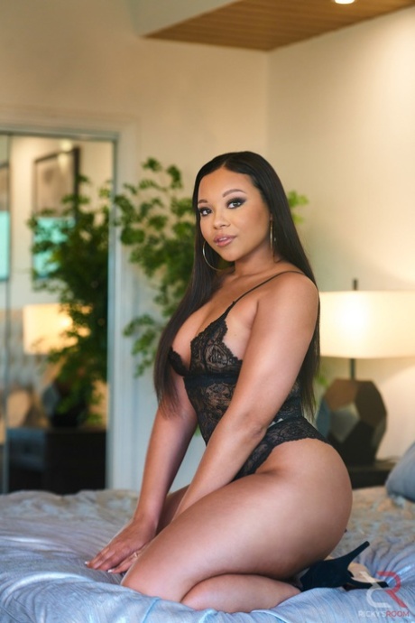 Curvy black beauty Adriana Maya models lingerie on a bed in heels